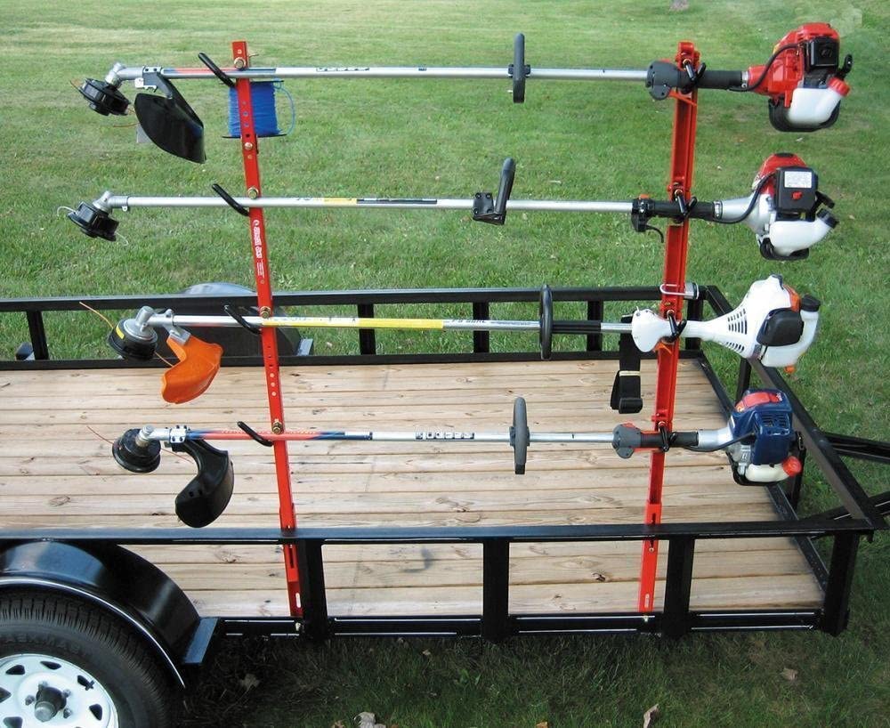 A set of red metal trimmer racks loaded with various lawn care tools on top of a trailer.